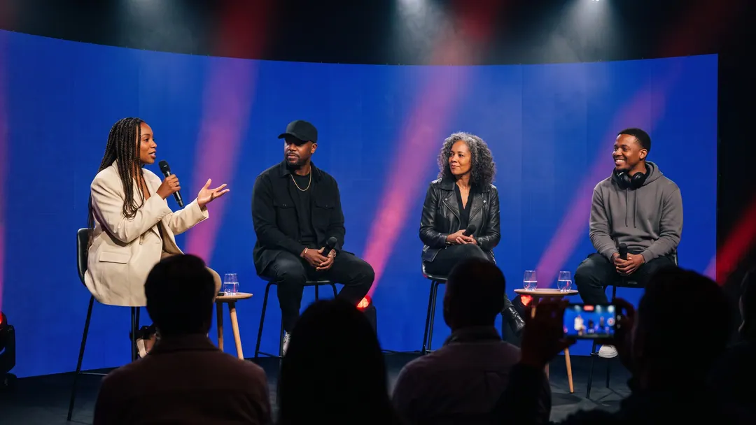 Illustrative image: four panelists in conversation on a stage in front of a blue LED wall.